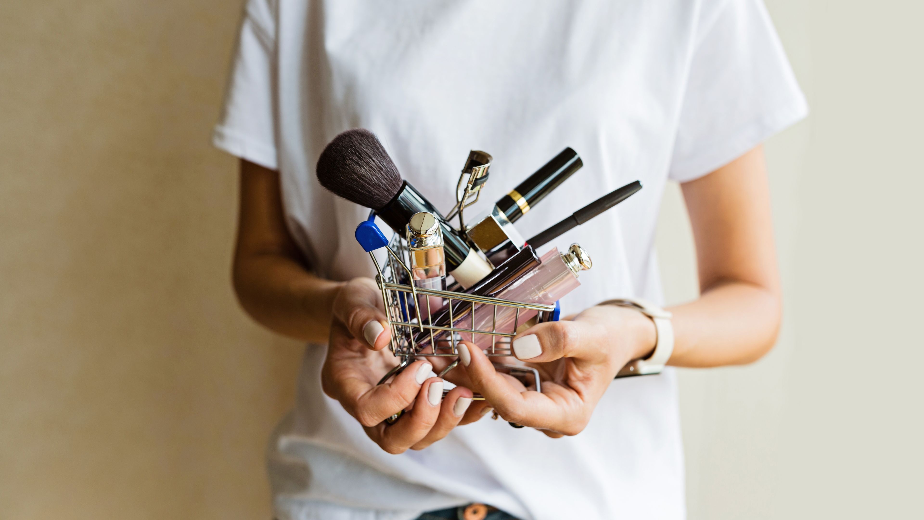 A woman holding a miniature shopping cart full of makeup products.